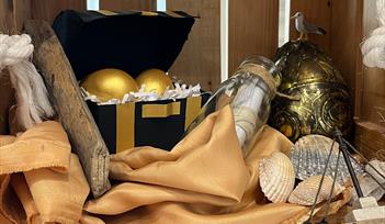 Chest with two golden eggs, message in glass bottle, ship, shells and big golden egg in crate.