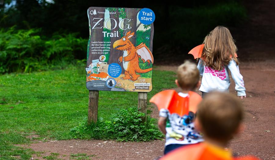 Children wearing orange cardboard dragon wings running towards a sign that says Zog Trail