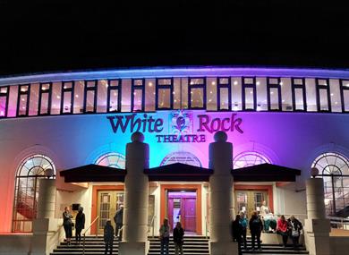 White Rock Theatre exterior lit at night with colourful lights and visitors gathered outside entrance.