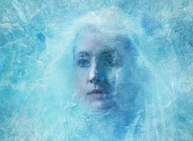 A woman frozen behind a sheet of ice - her hair is pulled out of her face to show her expression, also frozen in time.