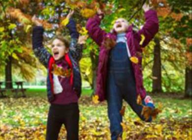 Two children having fun with autumn leaves at Sir Harold Hillier Gardens in Romsey, Hampshire