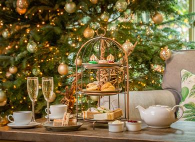 Festive afternoon tea with sandwiches, scones and sweet treats, served with tea and glasses of fizz beside a decorated Christmas tree.