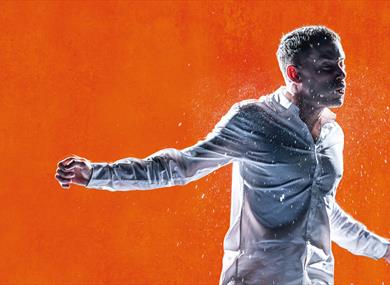 Against a bright orange background, a young man is in motion, as though mid-fight. He wears a white shirt. He holds one arm out to the side and his fa