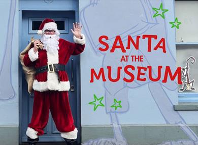 Santa dress in his Christmas costume standing in front of  a pale purple wall