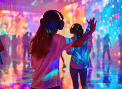 Two people wearing headphones dance in a colourful silent disco at Winchester Science Centre
