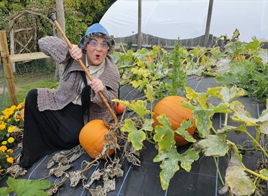 witchy woman crouching next to pumkins