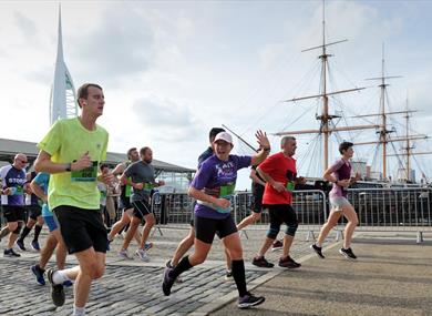 People running past HMS Warrior and the Spinnaker Tower in the Great South Run