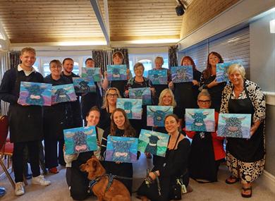 Painting party group holding finished paintings on canvases of Highland cows
