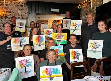 Painting party group holding finished paintings on canvases