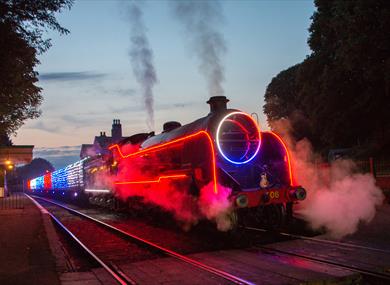 A steam locomotive travelling along a track with neon and fairy lights on the train.