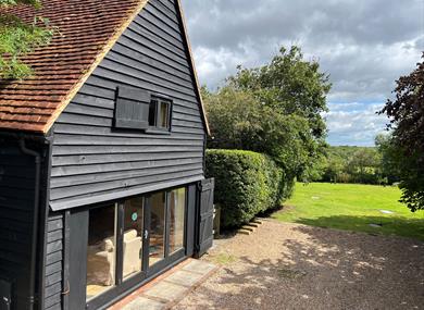 Black cladded barn with wide terrace doors. The view is a green field with trees in the far distance.