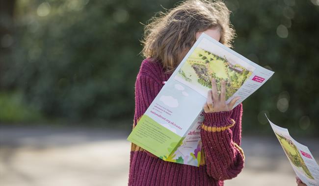 A young girl in a pink jumper writing on an Easter Trail sheet in the garden
