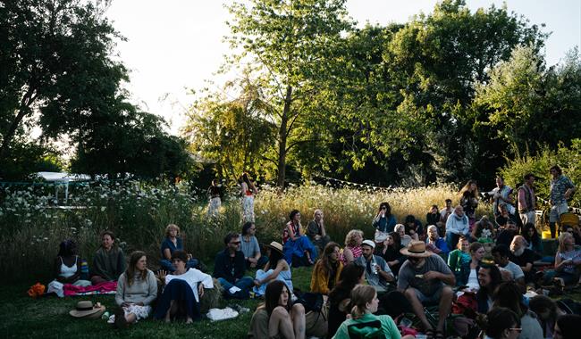 people sitting in the grass all together on picnic mats and chairs
