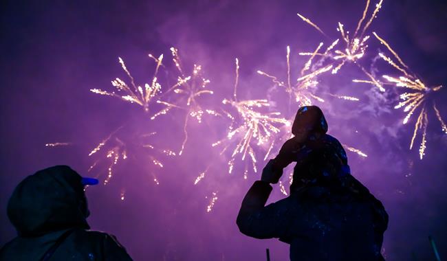 A family watching low bangs fireworks at Godstone Farm. The sky is purple and there are pretty fireworks. There is a lady and a man who has a child on