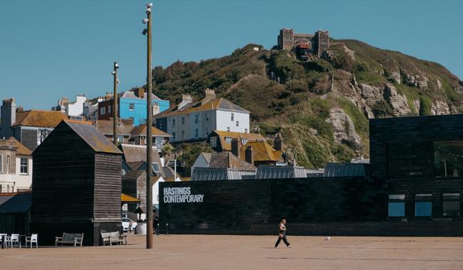 Hastings Contemporary gallery beneath East Hill cliffs, with Old Town buildings and fishing huts nearby.