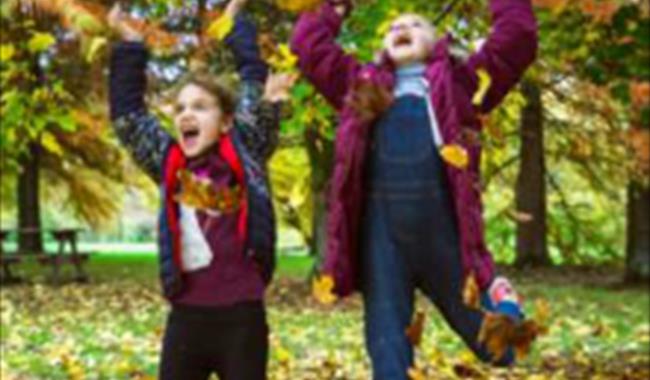 Two children having fun with autumn leaves at Sir Harold Hillier Gardens in Romsey, Hampshire