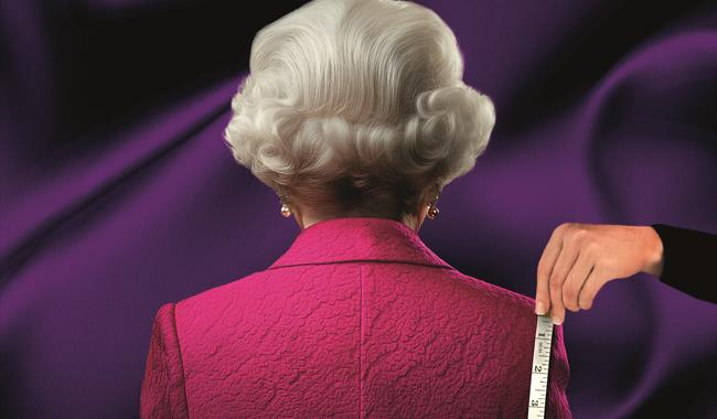 An imitation of Queen Elizabeth II from behind: an older woman with nearly styled, short, grey, wavy hair, pearl earrings and a pink jacket. A hand ho