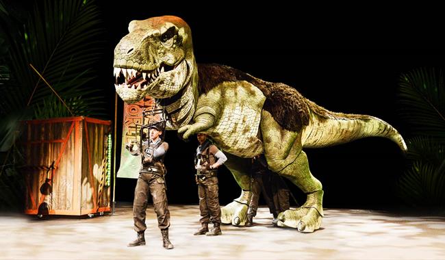 A huge green Tyrannosaurus Rex puppet operated by two puppeteers.