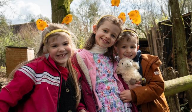 Three smiling children with Easter chick headbands at Chiltern Open Air Museum. One of the children is holding a cuddly sheep toy.