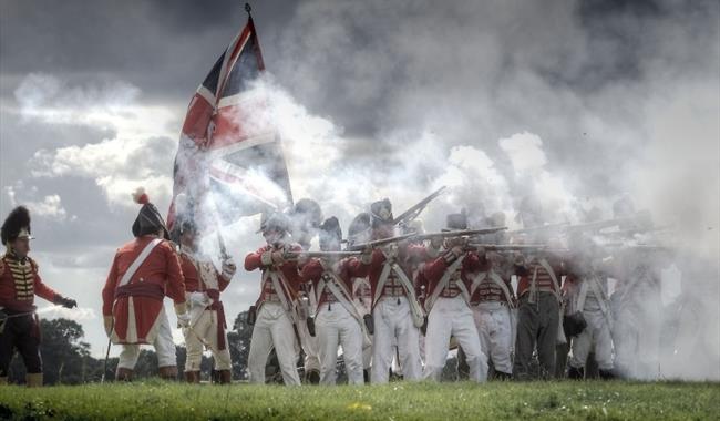 reenactors in napoleonic outfits holding muskets in a cloud of smoke
