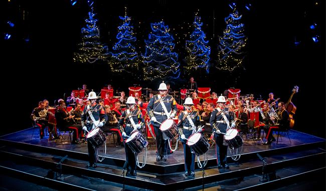 The Band of HM Royal Marines stand on the Festival Theatre stage dressed in military full dress, facing out front. Five drummers stand at the front, w