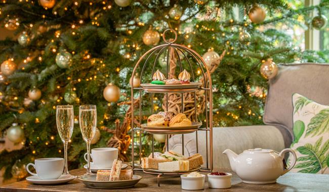 Festive afternoon tea with sandwiches, scones and sweet treats, served with tea and glasses of fizz beside a decorated Christmas tree.