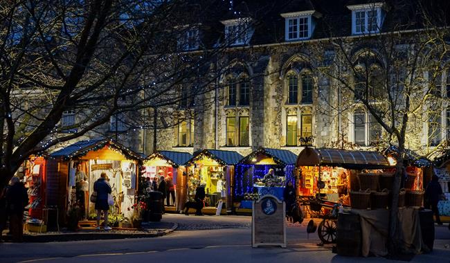 Winchester Cathedral Christmas Market chalets, with Winchester Cathedral in the background at night.