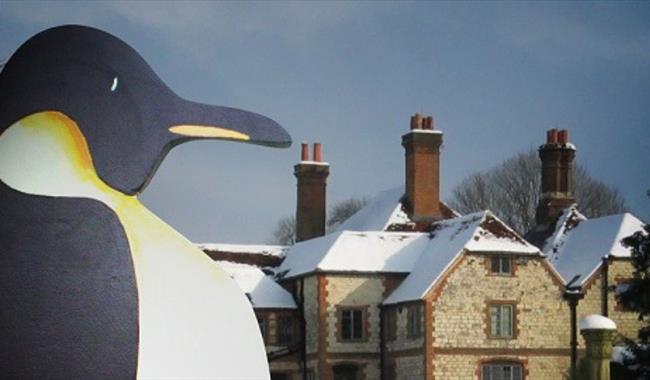 a penguin with Gilbert White's house covered in snow in the background