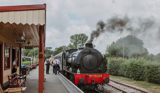 Kent and East Sussex Heritage Railway with a black steam locomotive at a station platform, emitting smoke.