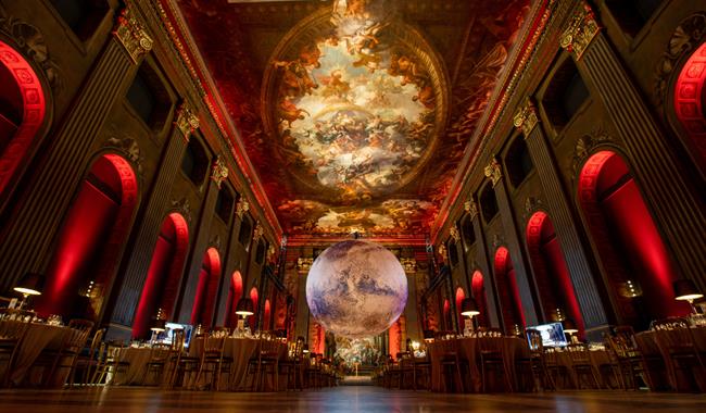 In a grand, ornate hall with a high, frescoed ceilings (the Painted Hall), a large, glowing model of planet Mars is suspended in the centre of the roo