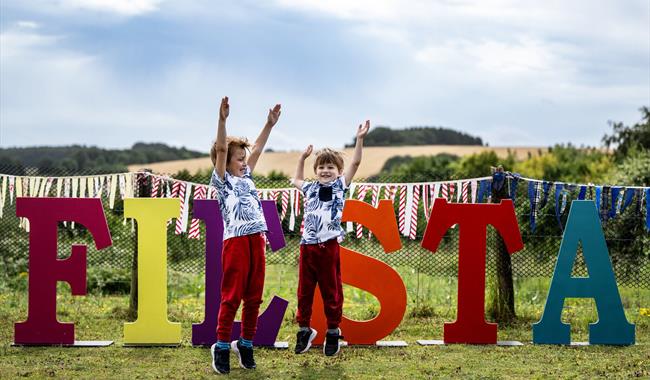 Two boys jumping in the air in front of big letters that spell 'Fiesta'