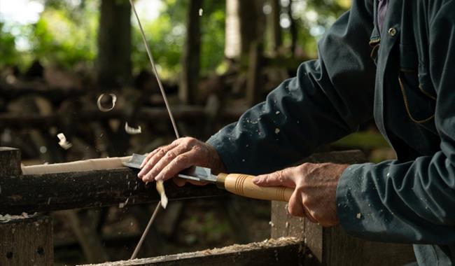 craftsman using chisel on turning piece of wooden leg