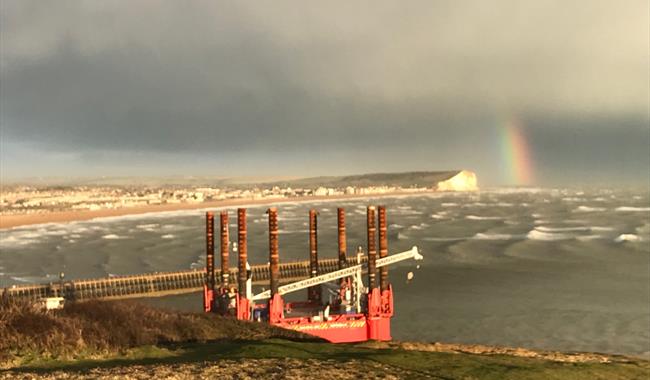 View over Seaford Bay with sunlit waves, dark clouds and a rainbow