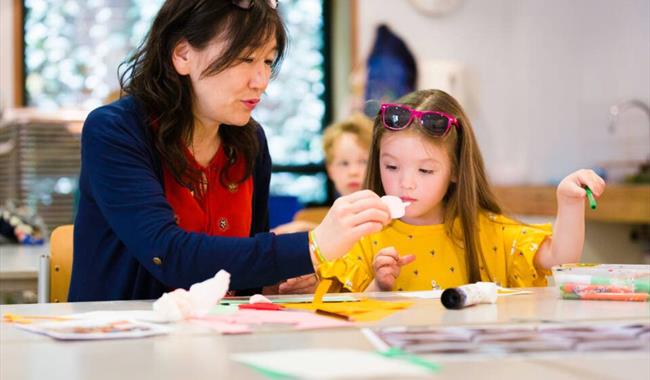 Adult and Child sitting at a table with art supplies. Adult is helping child with creating.