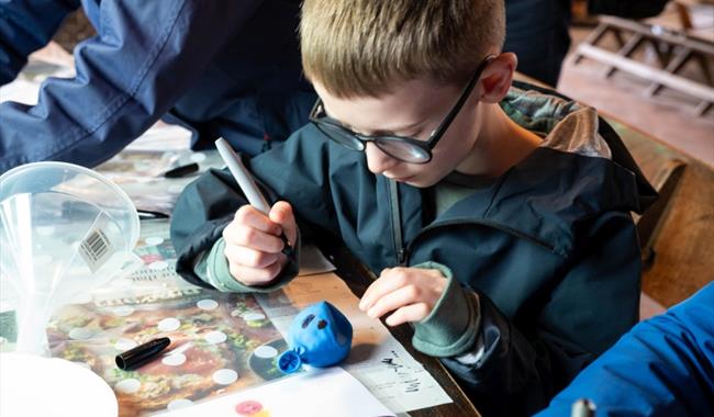 Boy in coat drawing a face on a sand filled balloon.