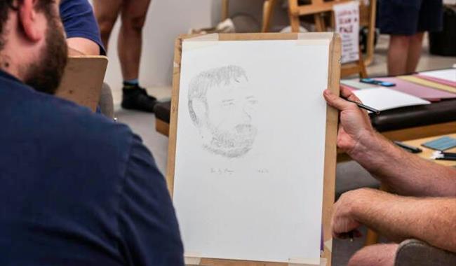 Drawing board being held for neighboring individual to look at with a pencil portrait drawing