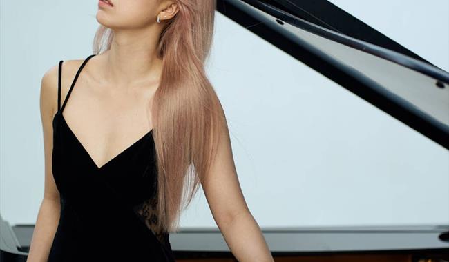 Pianist Fangwei Zhao in front of a grand piano