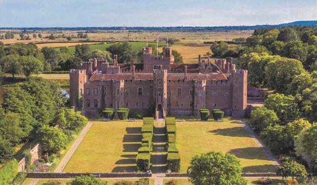 Aerial view of Herstmonceux Castle, highlighting its red-brick medieval architecture, symmetrical gardens, and surrounding greenery.