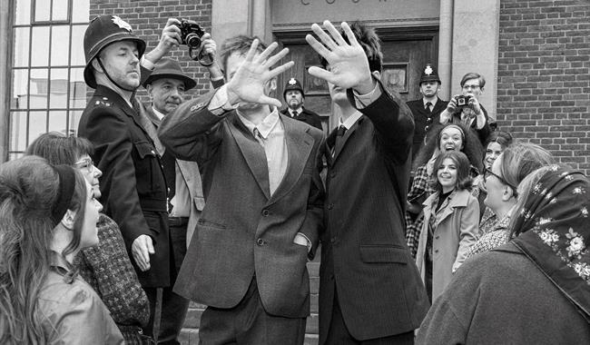 A black-and-white-photo taken on the crowded steps of Chichester Law Court. In the centre, two young men in stylish suits walk down the steps, holding