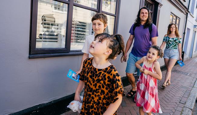 A group of people walking along a high street. There are two adults and three children.