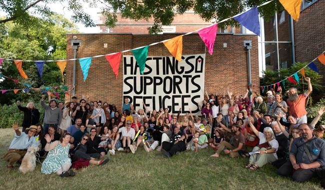 Crowd at Sanctuary Festival surround a large poster that reads 'Hastings supports Refugees'.