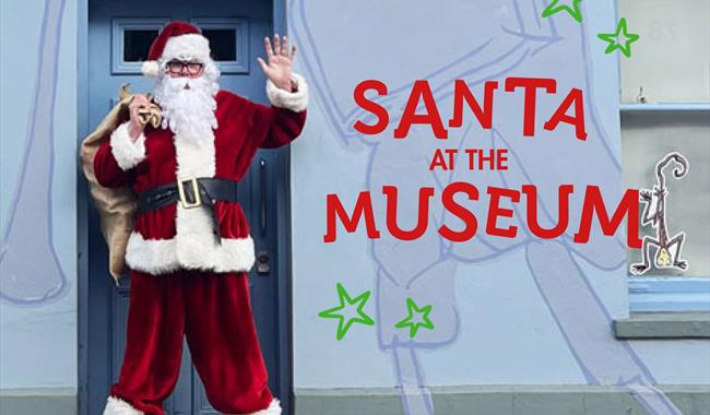 Santa dress in his Christmas costume standing in front of  a pale purple wall