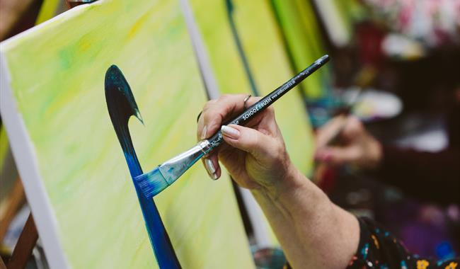 Close up of a canvas in a group setting with a red cup with paintbrushes in it