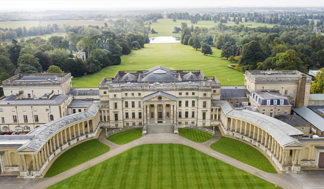 An aerial view of a large golden coloured palace with two wings that curve out either side of the main building held up with Grecian coloumns. The vie