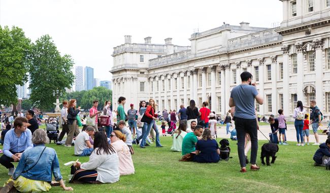 Groups of people hanging out in the lawns of the Old Royal Naval College, next to the Thames
