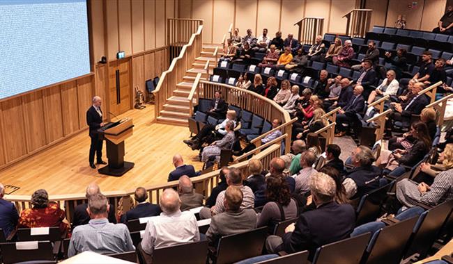 Inside the Fellowship Auditorium at Bletchley Park people are listening to a speaker.