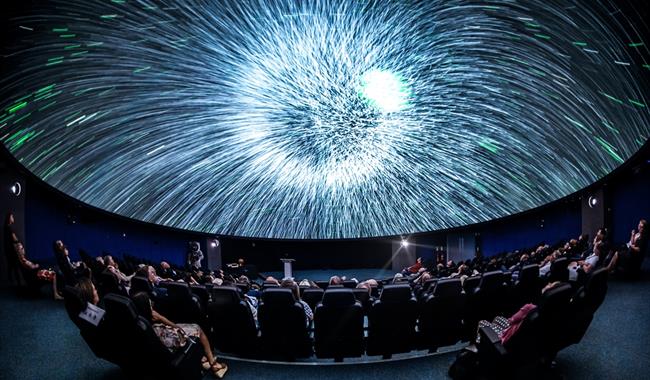 A blast of white light on a Planetarium dome. There are people sat in seats watching the screen.