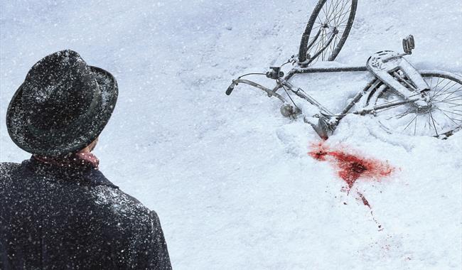 A black bicycle lies on the ground, half covered in snow. Next to the bike, a patch of snow is stained red with blood. In the foreground, a man is tur