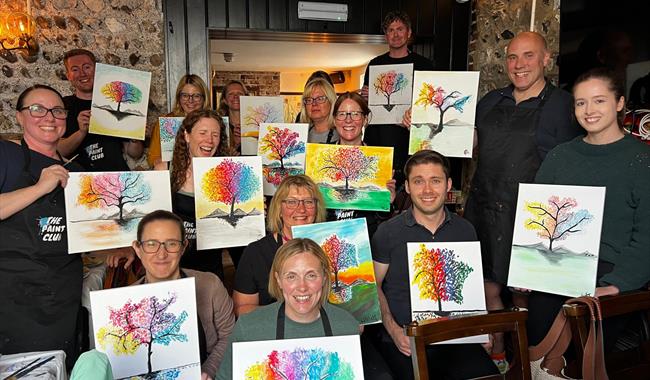 Painting party group holding finished paintings on canvases