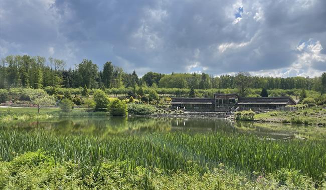 A view across water to a wooden one story building surrounded by trees.